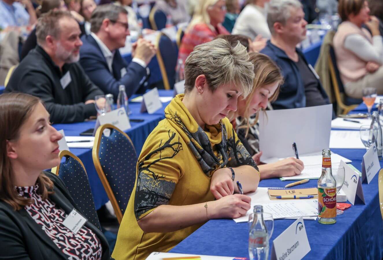 Das Foto zeigt Teilnehmende bei der BIH-Fachtagung 2024 EAA-Netzwerktreffen. Mehrere Personen schreiben Notizen auf ihren Block, andere hören interessiert zu.