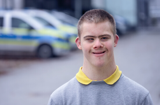 Portraitfoto von Dominik. Im Hintergrund mehrere Polizeiautos.