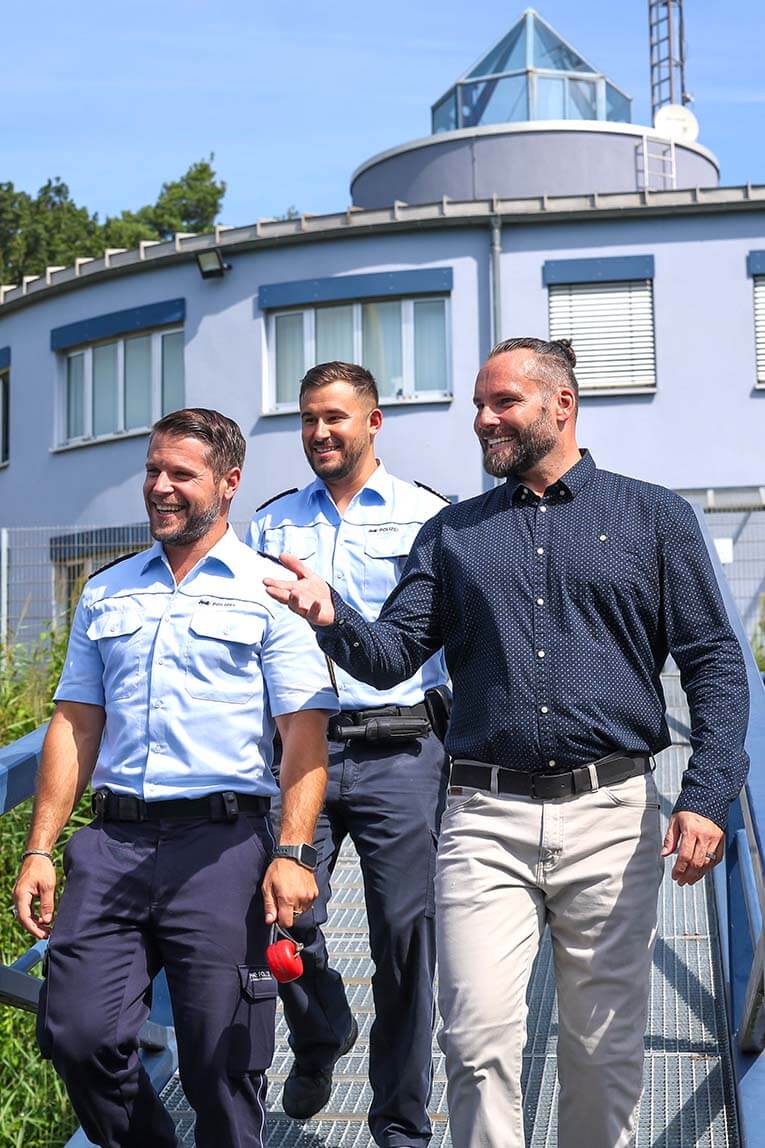 Drei Polizisten gehen eine Landungsbrücke herunter, dahinter ist ein Gebäude zu sehen.