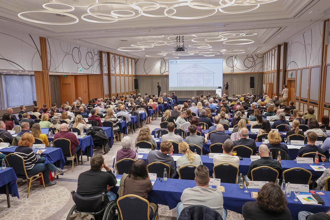 Ein vollbesetzter Saal von hinten zur Bühne hin fotografiert.