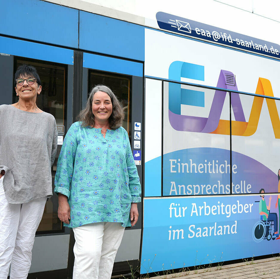 Kisten-Susanne-Dier (rechts) steht vor einem Zugwaggon, der mit dem Logo der EAA Saarland bedruckt ist.